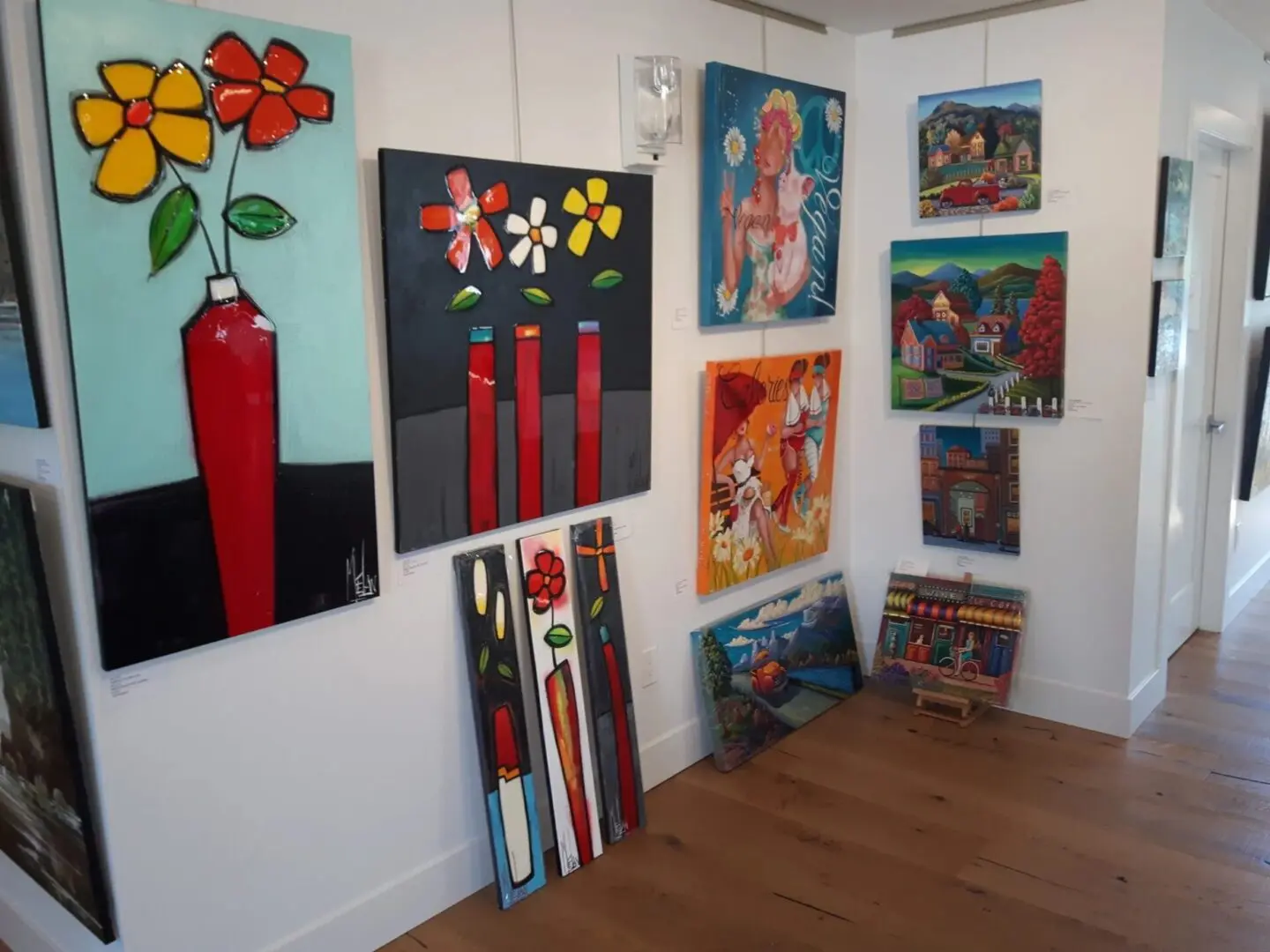 A small gallery showcases vibrant paintings of flowers, buildings, and landscapes, arranged on white walls and wooden floors.