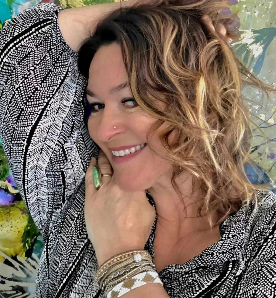 Smiling woman with curly hair and jewelry.
